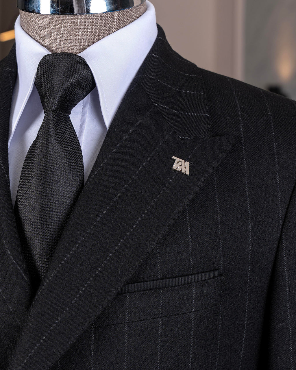 Close-up of a black stripe suit with a wooden hand wearing a white shirt cuff, featuring a 'French Cuff' label.